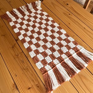 K&ouml;nnte beinhalten: Ein brauner und wei&szlig;er karierter Tischl&auml;ufer mit Fransen an den R&auml;ndern. Der L&auml;ufer ist aus gewebter Baumwolle und perfekt, um Ihrem Esstisch einen Hauch von Landhausstil zu verleihen.