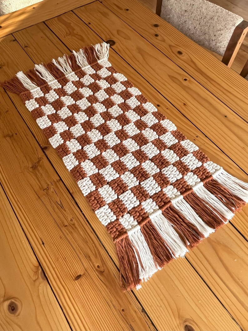 K&ouml;nnte beinhalten: Ein brauner und wei&szlig;er karierter Tischl&auml;ufer mit Fransen an den R&auml;ndern. Der L&auml;ufer ist aus gewebter Baumwolle und perfekt, um Ihrem Esstisch einen Hauch von Landhausstil zu verleihen.