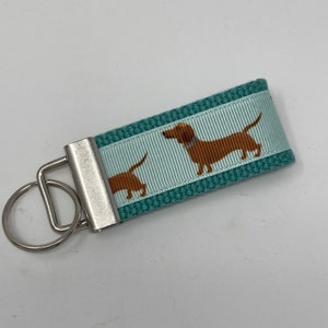 May include: Teal blue key chain with a silver key ring and a white and teal striped ribbon with a brown dachshund dog print.