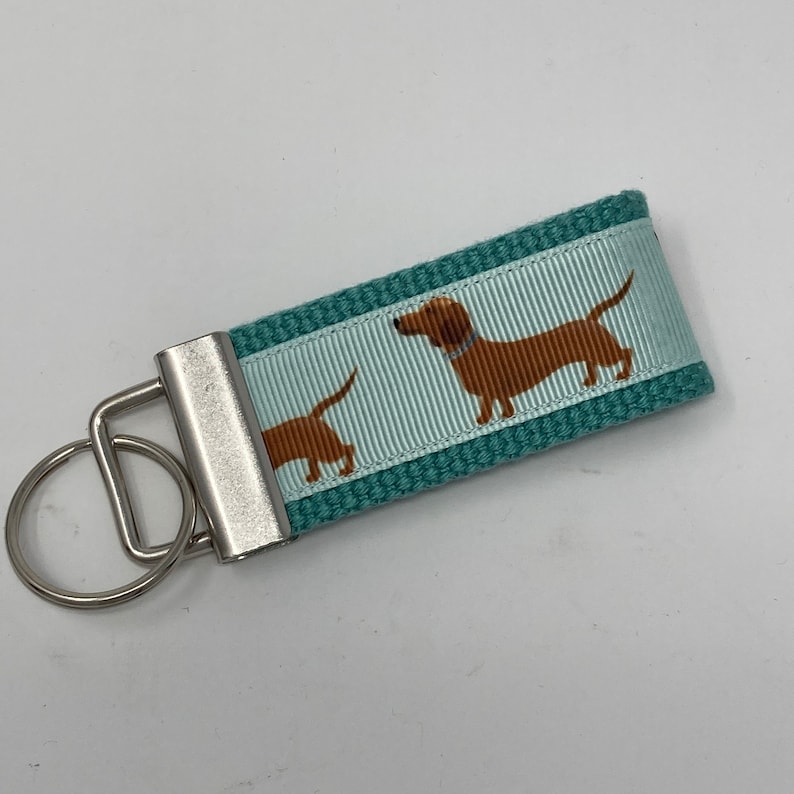 May include: Teal blue key chain with a silver key ring and a white and teal striped ribbon with a brown dachshund dog print.