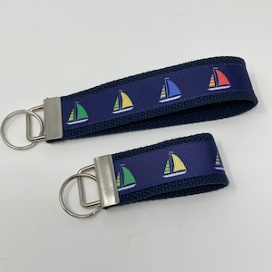 May include: Two navy blue keychains with silver key rings. The keychains are made of fabric with a repeating pattern of colorful sailboats.