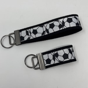 May include: Two black and white soccer ball patterned keychains with silver key rings. The larger keychain is about 5 inches long and the smaller keychain is about 3 inches long.