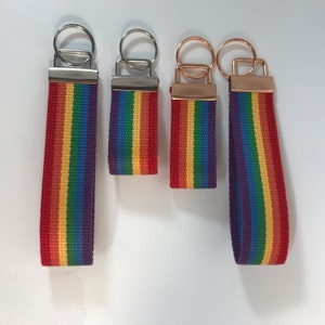 K&ouml;nnte beinhalten: Vier regenbogenfarbene Schl&uuml;sselanh&auml;nger mit silbernen und goldenen Schl&uuml;sselringen. Die Schl&uuml;sselanh&auml;nger sind aus gewebtem Stoff mit roten, orangen, gelben, gr&uuml;nen, blauen und violetten Streifen.
