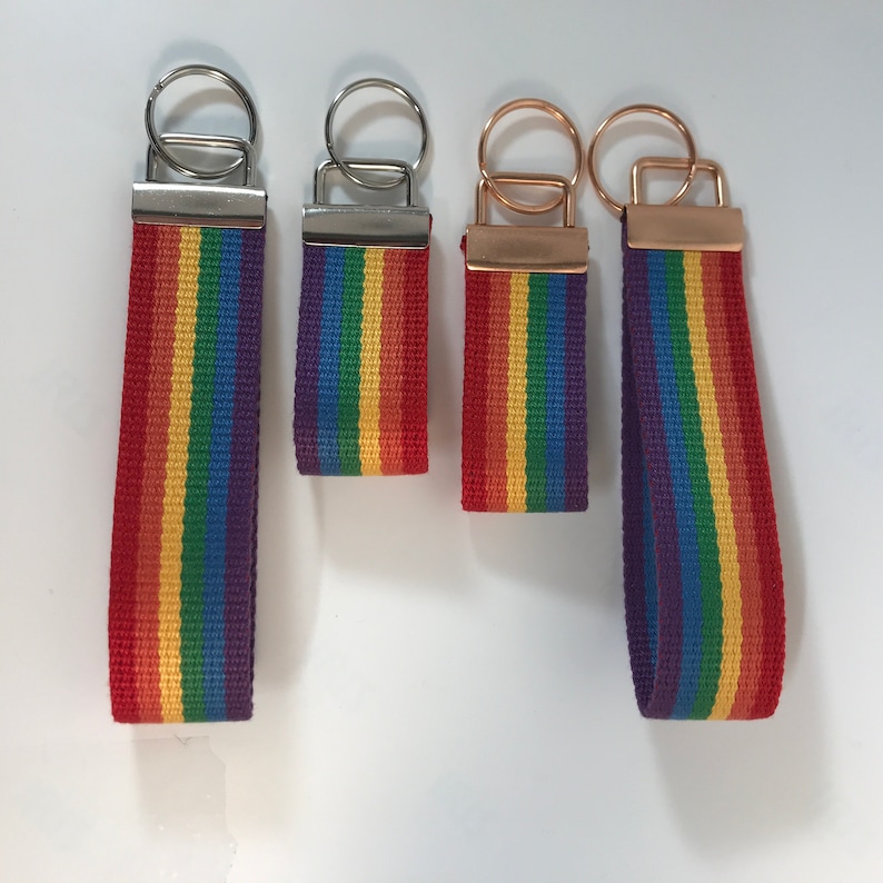 K&ouml;nnte beinhalten: Vier regenbogenfarbene Schl&uuml;sselanh&auml;nger mit silbernen und goldenen Schl&uuml;sselringen. Die Schl&uuml;sselanh&auml;nger sind aus gewebtem Stoff mit roten, orangen, gelben, gr&uuml;nen, blauen und violetten Streifen.