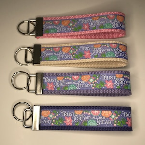 May include: Four keychains with floral designs and the text "Trust in the Lord with all your heart". The keychains are in pink, beige, purple, and a darker purple.