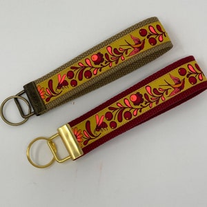 May include: Two keychains with gold key rings. One keychain is brown with a yellow, pink, and red floral pattern. The other keychain is burgundy with a yellow, pink, and red floral pattern.