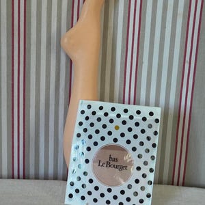 May include: A white package with black polka dots and the text "bas Le Bourget" in a circle. The package is on a white surface with red and white stripes.