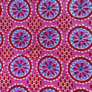 Könnte beinhalten: Rosafarbener Stoff mit einem sich wiederholenden Muster aus roten, blauen und violetten Kreisen. Die Kreise haben einen weißen Umriss und ein geometrisches Design im Inneren.