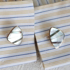 May include: A pair of silver cufflinks with a white and black mother-of-pearl design.