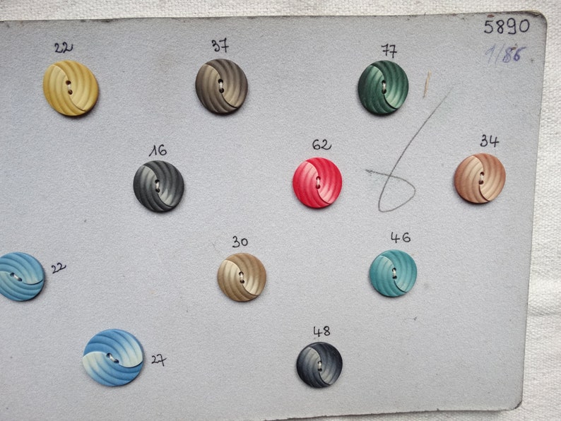 May include: A collection of decorative buttons in various colors, including yellow, gray, green, red, and blue. Each button has a spiral design and two holes for sewing. Numbers are printed next to each button. The number "5890 1/86" is printed in the upper right corner.