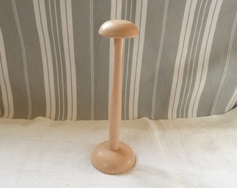 May include: A light pink wooden hat stand with a round top and a tall, slender base.