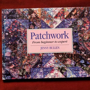 May include: A hardback book titled Patchwork: From beginner to expert by Jenny Bullen. The cover features a vibrant, multi-coloured floral and paisley patchwork quilt pattern in shades of blue, purple, pink, and black with a central pink label.