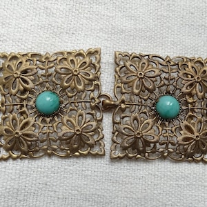 May include: A pair of gold-tone metal belt buckles with intricate floral designs and turquoise-coloured glass stones.
