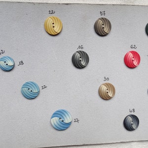 May include: A collection of round, spiral-designed buttons in various colors, including yellow, gray, red, blue, and green. Each button has a number next to it. The buttons are arranged on a light gray surface.