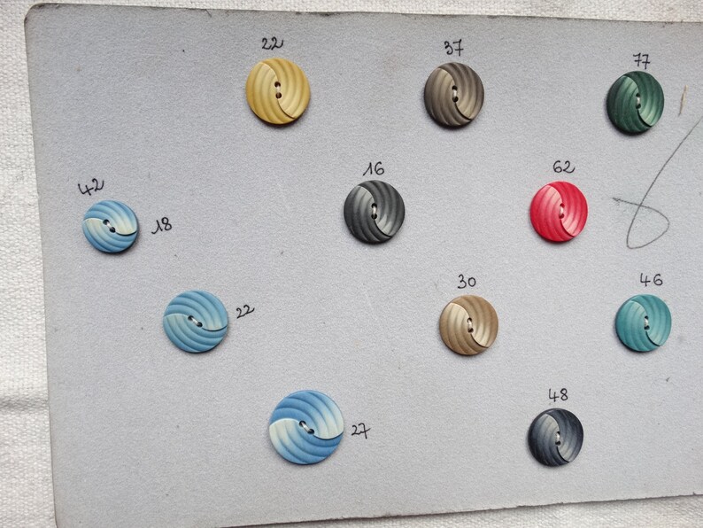 May include: A collection of round, spiral-designed buttons in various colors, including yellow, gray, red, blue, and green. Each button has a number next to it. The buttons are arranged on a light gray surface.