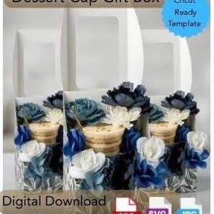May include: A digital download template for a Dessert Cup Gift Box, featuring a Cricut Ready Template label. The image displays three white boxes with clear windows, each containing a dessert cup decorated with blue and white artificial flowers.
