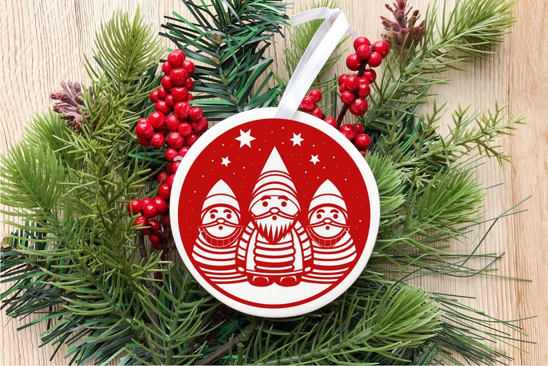 May include: A red and white Christmas ornament featuring three white gnomes with red hats and beards. The gnomes are standing in a row with stars in the background.