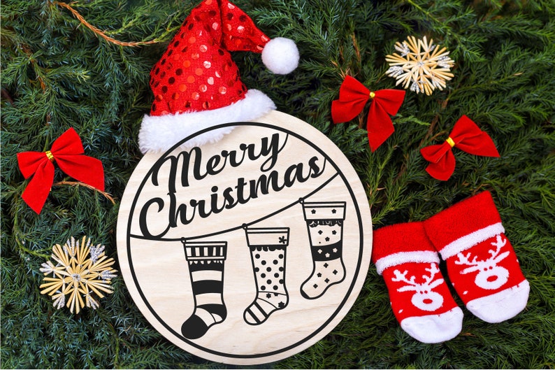 May include: A round wooden sign with the text "Merry Christmas" in black script. Three black and white stockings are hanging from a string with clothespins. The sign is surrounded by green pine branches, red bows, and a red Santa hat.