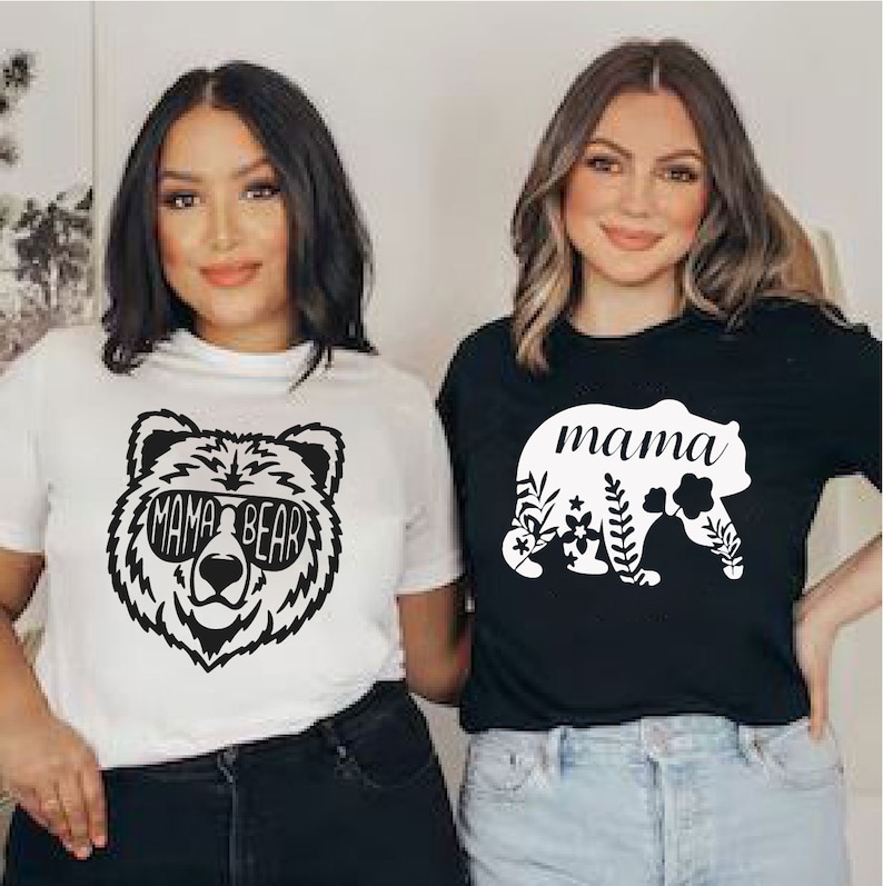 Puede incluir: Dos mujeres con camisetas a juego. Una camiseta es blanca con un gr&aacute;fico de oso negro con gafas de sol y las palabras "MAMA BEAR". La otra camiseta es negra con un gr&aacute;fico de oso blanco y la palabra "mama" dentro del oso.