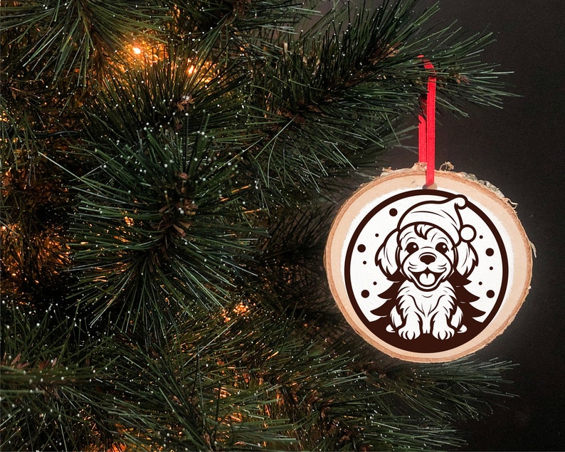 May include: A round wooden Christmas ornament with a white silhouette of a dog wearing a Santa hat. The ornament is hanging from a red ribbon on a green Christmas tree.