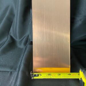 May include: A brushed copper sheet measuring 4 inches wide by 12 inches long. The sheet is being measured with a yellow tape measure.