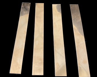 May include: Four thin, rectangular strips of metal, all the same size, are arranged in a row. The metal is a light gold color and has a slightly textured surface.