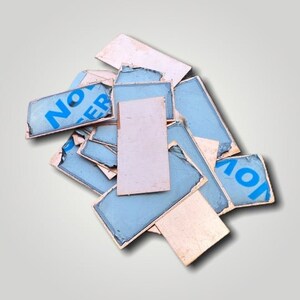 May include: A pile of rectangular, weathered stickers with a light blue background and white text that reads "NO" and "ER". Some stickers are plain white. The stickers have a distressed, vintage appearance.