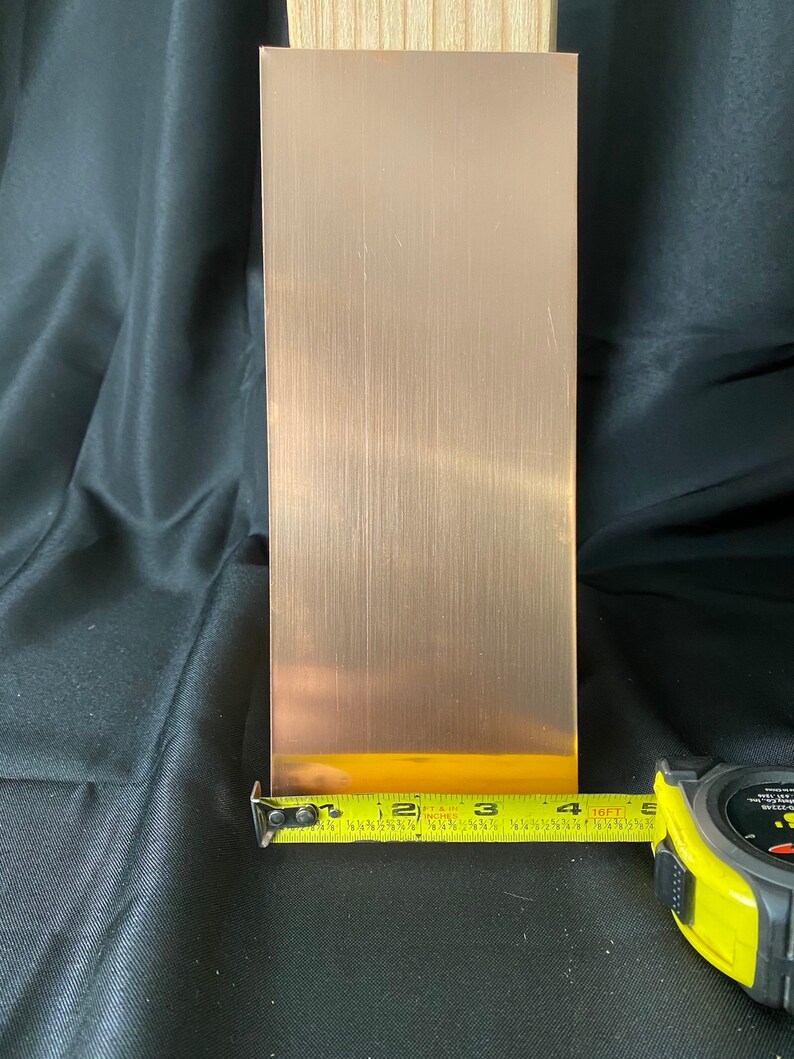 May include: A brushed copper sheet measuring 4 inches wide by 12 inches long. The sheet is being measured with a yellow tape measure.