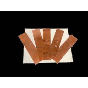 May include: Five thin strips of copper foil, arranged in a fan shape on a white surface.