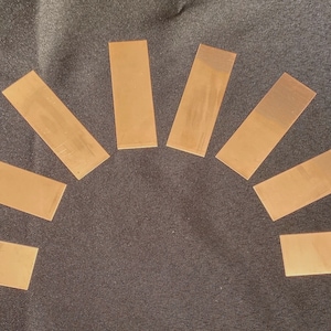 May include: Eight rectangular pieces of copper foil arranged in a semi-circle on a dark gray fabric background.