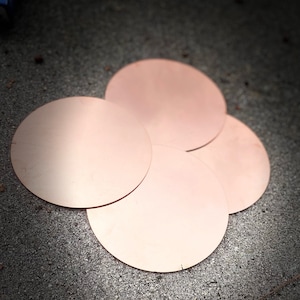 May include: Four copper-colored, circular discs are arranged on a textured, gray surface. The discs are evenly spaced, with a slight overlap, and appear to be made of a smooth, reflective material. The lighting creates highlights and shadows on the surfaces.