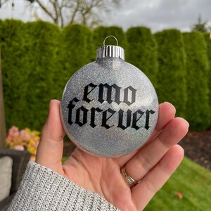 May include: Silver glitter Christmas ornament with the text "emo forever" in black gothic font.