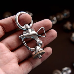 May include: A silver swivel snap hook with a wooden base. The hook is attached to a metal ring.