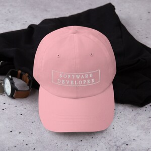 Puede incluir: Una gorra de b&eacute;isbol rosa con un rect&aacute;ngulo blanco bordado que dice "SOFTWARE DEVELOPER".
