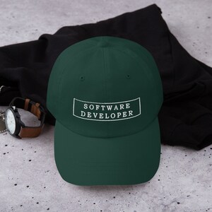 Puede incluir: Una gorra de b&eacute;isbol verde oscuro con un rect&aacute;ngulo blanco bordado que dice "SOFTWARE DEVELOPER".