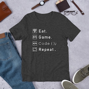 Op de afbeelding: Donkergrijs t-shirt met een witte afbeelding met de tekst "Eten. Gamen. Coderen(); Herhalen."