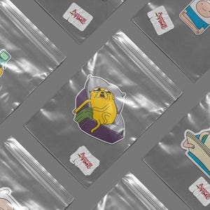 May include: Several clear plastic bags, each containing an Adventure Time sticker. The stickers depict characters such as Jake the Dog and Finn the Human. Some stickers include the text "I Love You, Jake".
