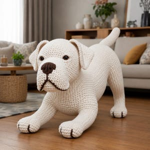May include: A cream-colored crochet dog figurine in a playful stance with its front legs extended. The dog features a dark brown nose, dark brown mouth detailing, dark brown paw accents, and round dark eyes, all crafted with a textured yarn stitch.