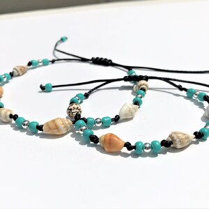 May include: Two adjustable bracelets featuring turquoise and silver beads, along with seashells. The bracelets are made with black cord.