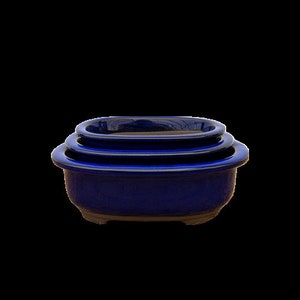 May include: A set of three nesting ceramic bowls in a deep blue glaze. The bowls are oval-shaped with a slightly raised rim and a textured, unglazed base. The bowls are designed to nest inside each other for compact storage.