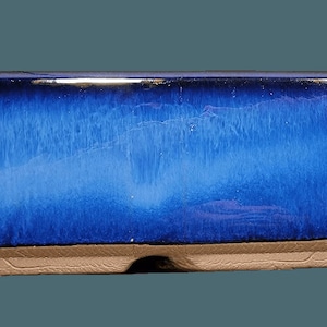 May include: A blue ceramic rectangular bonsai pot with a glazed finish. The pot has a slightly rounded bottom and a drainage hole.