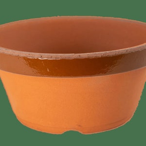 May include: A terracotta flower pot with a brown glazed rim. The pot is empty and ready for planting.