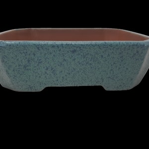 May include: A square bonsai pot with a speckled teal exterior and a brown interior. The pot has a low profile with a slightly angled design and two small feet on the bottom. The pot is empty.