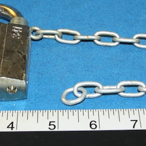 May include: A silver padlock with a silver chain attached. The padlock has a keyhole and a silver key is next to it. The padlock is 2 inches wide and the chain is 10 inches long.