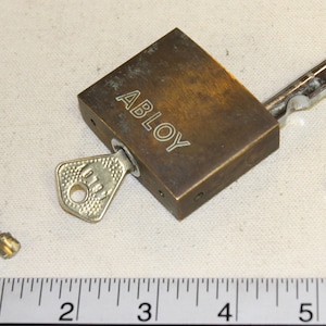 Puede incluir: Un candado de latón con un grillete de plata y dos llaves. El candado está etiquetado como "ABLOY".