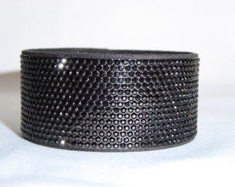 May include: A black leather bracelet with a black rhinestone design.