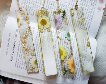 May include: Five handmade bookmarks with pressed flowers and gold leaf accents. Each bookmark features a different flower and inspirational quote. The bookmarks are made of clear resin and have a gold tassel.