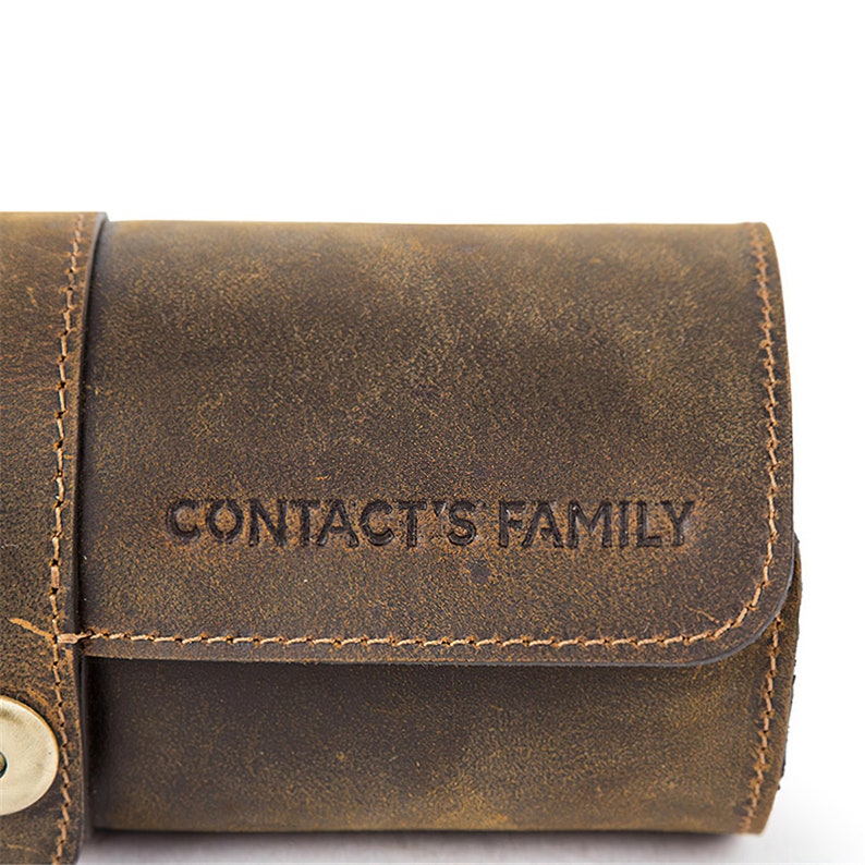 Peut inclure: Un &eacute;tui enroulable en cuir marron avec le texte "CONTACT'S FAMILY" en relief sur le devant.