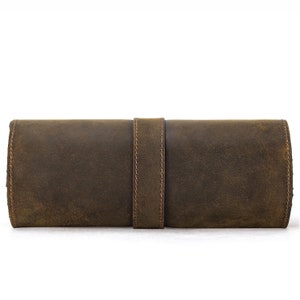 Peut inclure: Un &eacute;tui enroulable en cuir marron avec une sangle cousue. L'&eacute;tui est en cuir vieilli et a un aspect rustique.