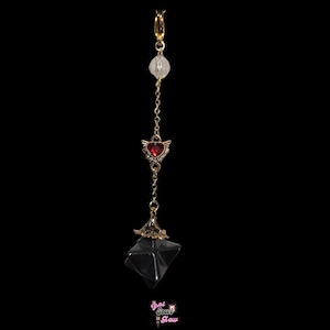 May include: A gold-colored belly button ring with a clear crystal bead, a red heart with wings, and a faceted black crystal pendant. The ring is suspended from a chain and has a clasp at the top. The text "That Soul Glow" is at the bottom.